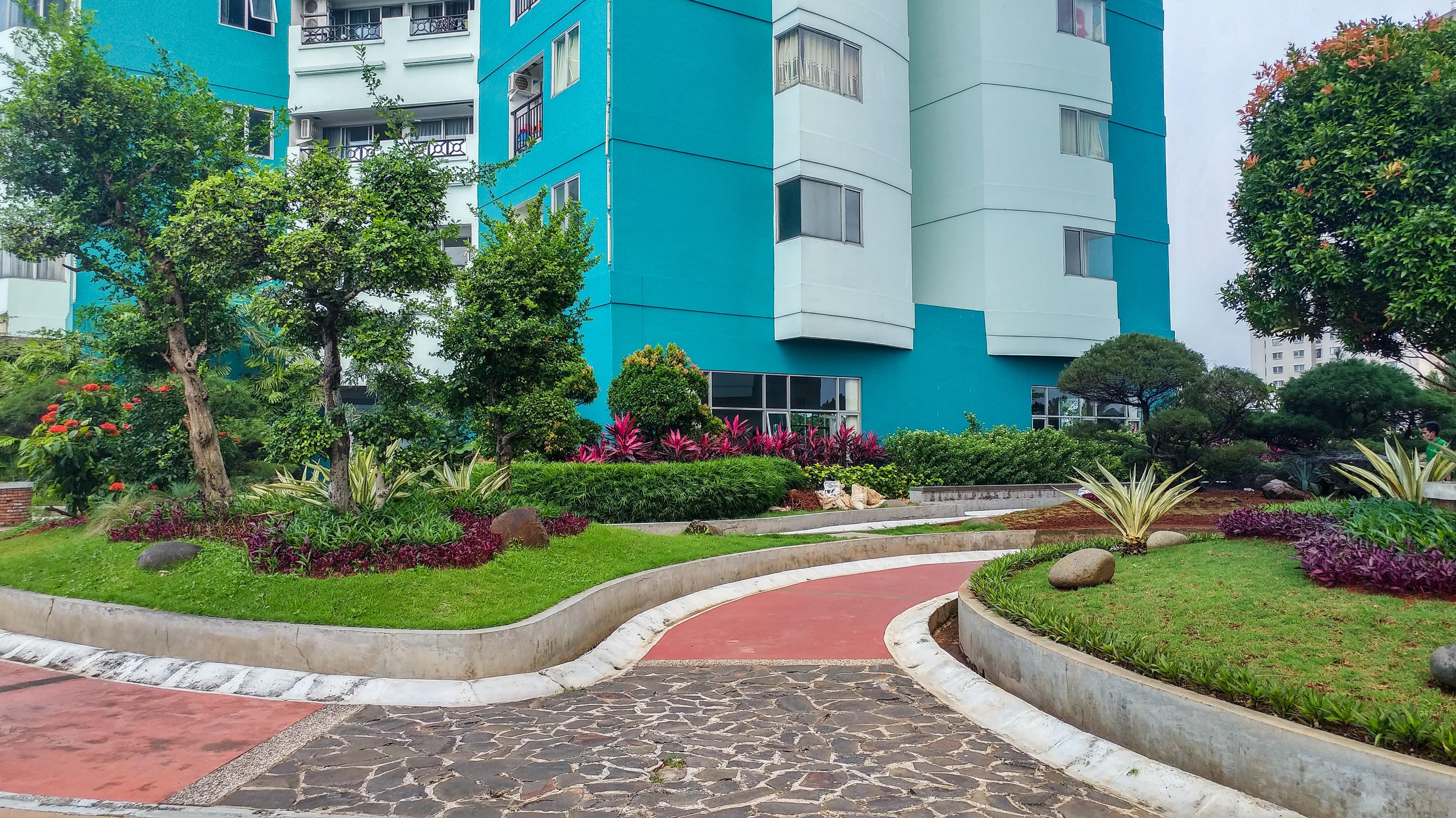 Taman dan jalur pejalan kaki di area Green Central City, dengan tanaman hias tertata rapi di kaki tower apartemen