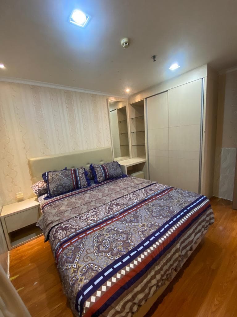 Kamar tidur dengan ranjang, lemari pakaian pintu geser bercermin, dan meja nakas di unit sewa Green Central City