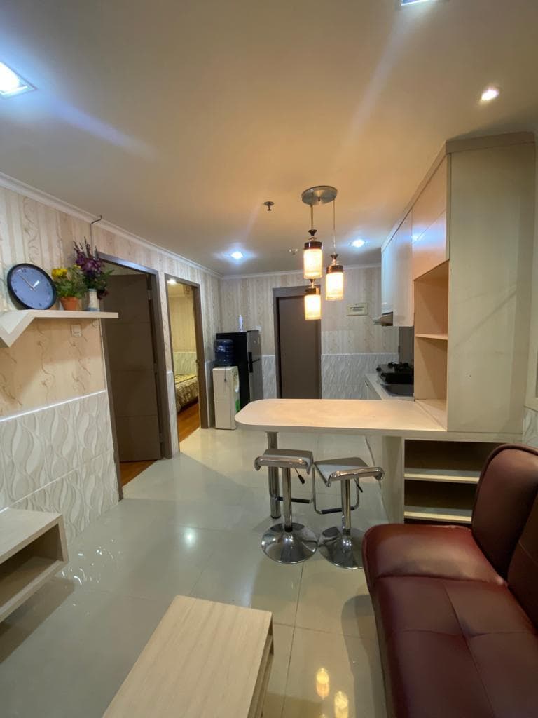 Meja bar dengan dua kursi, kulkas, dan dispenser air di dekat pintu kamar tidur unit Green Central City